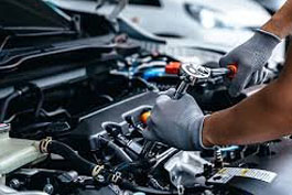 A mechanic wearing gloves uses a ratchet wrench to repair an engine under a car hood, focused on mechanical components.