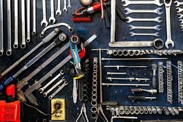 A flat lay of various hand tools, including wrenches, sockets, and pliers, organized neatly on a dark background.