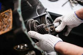 A technician in white gloves carefully assembles metal gears within a mechanical device during repair.